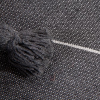 Długi pled bawełniany w kolorze grafitowym w paski. Ręcznie tkana narzuta z chwostami. Stylowy bieżnik na łóżko i sofę.